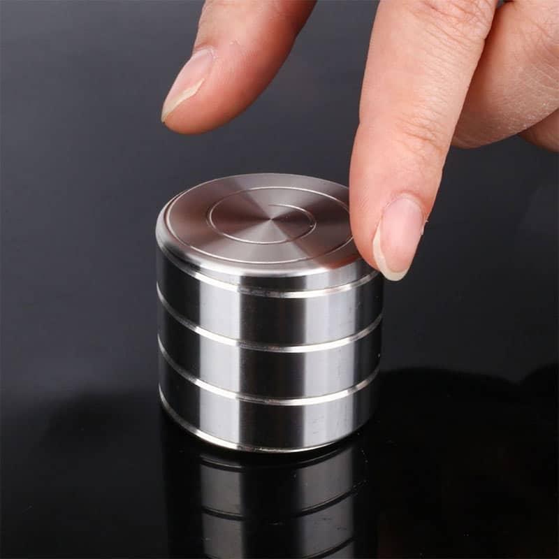 Pièce métallique cylindrique en acier inoxydable, empilée, avec une main pointant vers le haut, sur fond noir.