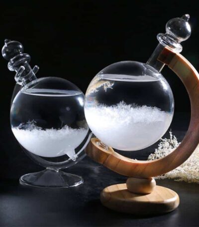Vase en verre contenant un liquide transparent avec des cristaux ou des particules, posé sur une base en bois courbée, avec un fond noir pour mettre en valeur l'objet.