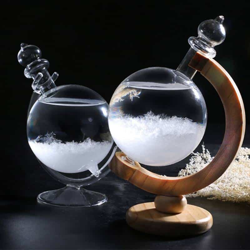 Vase en verre contenant un liquide transparent avec des cristaux ou des particules, posé sur une base en bois courbée, avec un fond noir pour mettre en valeur l'objet.