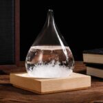 Pendentif en verre en forme de goutte d'eau contenant un liquide transparent, posé sur une base en bois, idéal pour la décoration scientifique ou comme accessoire original.