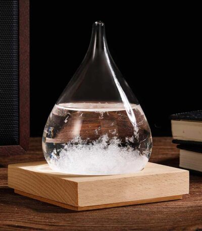Pendentif en verre en forme de goutte d'eau contenant un liquide transparent, posé sur une base en bois, idéal pour la décoration scientifique ou comme accessoire original.