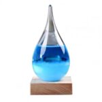 Pipette en verre contenant un liquide bleu, posée sur un socle en bois, utilisée comme objet de décoration scientifique ou pour des expériences éducatives.