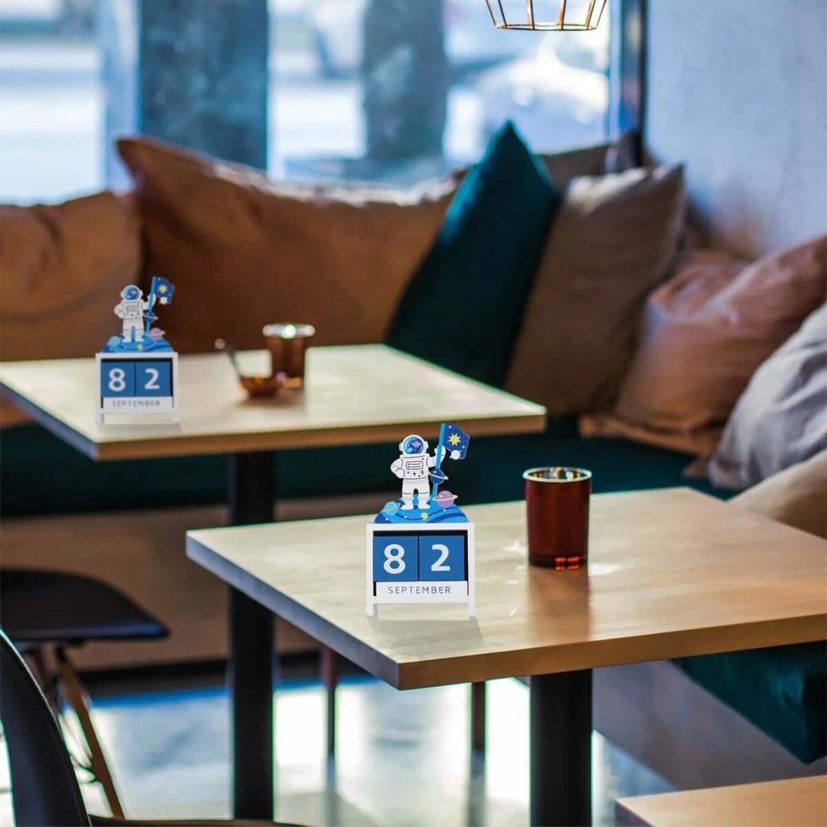 Décoration de table avec calendrier scientifique astronautes, affichant la date 8 septembre, dans un café cosy avec coussins et lumière naturelle.