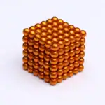 Puce magnétique en forme de cube doré, composée de petites sphères métalliques brillantes empilées pour créer un objet décoratif ou scientifique.