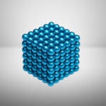 Modèle de cube composé de nombreuses billes métalliques bleues brillantes empilées en forme de cube, avec un fond neutre.