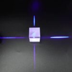 Porte-laser en verre transparent avec lumière bleue, projetant des lignes lumineuses sur une surface noire, créant un effet visuel futuriste et scientifique.