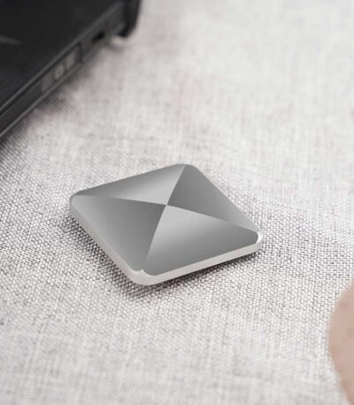 Panneau de stockage portable en aluminium gris, compact et moderne, posé sur une surface en tissu clair, à côté d’un ordinateur portable.
