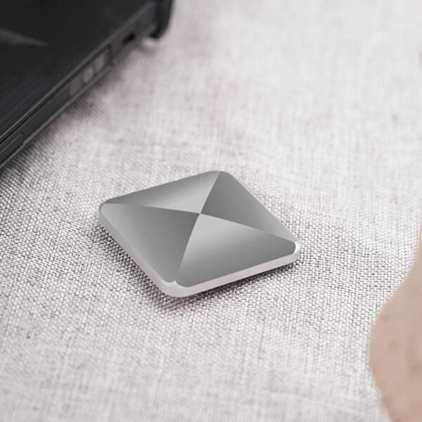 Panneau de stockage portable en aluminium gris, compact et moderne, posé sur une surface en tissu clair, à côté d’un ordinateur portable.