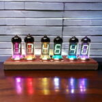 Nombres lumineux en verre coloré affichant les chiffres 1, 2, 3, 4, 5 et 6, posés sur un support en bois, avec un fond en briques blanches.