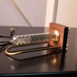 Pédale de phonographe vintage avec tube en verre et base en bois, illustrant un objet scientifique ancien utilisé pour la lecture de disques vinyles.