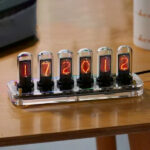 Horloge Nixie vintage avec six tubes lumineux affichant la date 17/12/2021, posée sur une table en bois, style rétro et technologique.