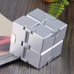 Cube puzzle métallique en forme de casse-tête, composé de plusieurs pièces interconnectées, posé sur une surface en bois avec une plante verte en arrière-plan.