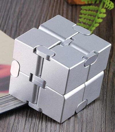 Cube puzzle métallique en forme de casse-tête, composé de plusieurs pièces interconnectées, posé sur une surface en bois avec une plante verte en arrière-plan.