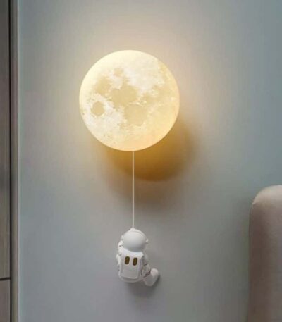 Lampe murale en forme de lune avec figurine d'astronaute suspendue, créant une ambiance spatiale et chaleureuse dans la pièce.