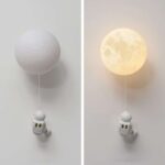 Lampe murale en forme de lune avec un petit astronaute suspendu, idéale pour une décoration originale et éducative.