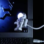 Vaisseau spatial en plastique blanc avec casque lumineux, suspendu devant un écran d'ordinateur, illustrant un thème scientifique et spatial pour la décoration ou la collection.