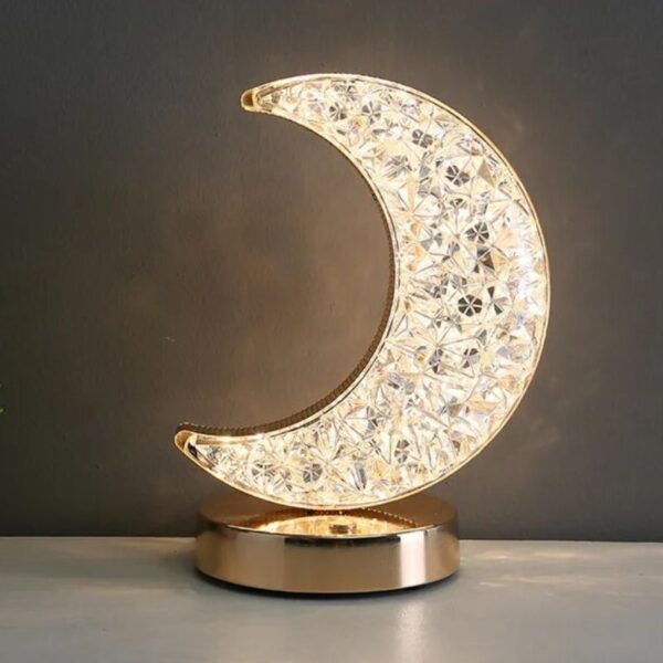 L'ampoule en forme de lune en cristal, élégante et raffinée, repose sur une base en métal doré, idéale pour une décoration de style scientifique ou moderne.