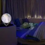 Lampe de décoration en forme de planÚte Terre illuminée, posée sur une table à cÎté d'un lit rond avec deux enfants qui jouent et se détendent dans une ambiance chaleureuse et cosy.