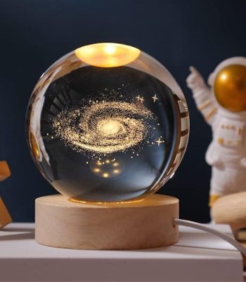 Boule en verre contenant une galaxie miniature avec étoiles et poussière cosmique, posée sur un socle en bois, idéale pour la décoration d'intérieur à thème scientifique ou cosmologique.