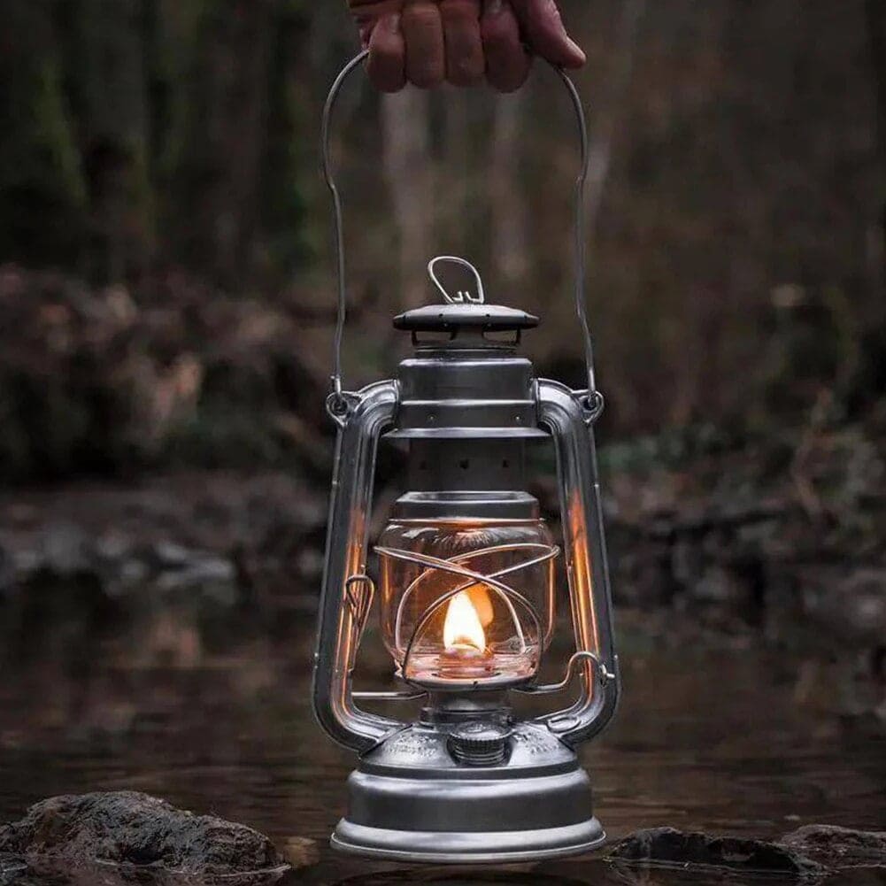 Lampe à pétrole en métal avec flamme allumée, suspendue au-dessus d'une rivière dans un environnement forestier.
