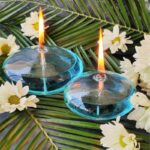 Ampoules flottantes en verre avec flammes allumées, entourées de fleurs blanches et de feuilles vertes tropicales.