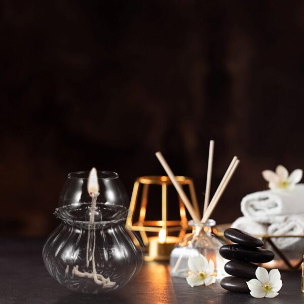 Bougie flottante en verre avec flamme allumée, décor zen avec pierres noires et fleurs blanches, ambiance relaxante pour décoration intérieure ou spa.