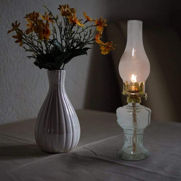Baladez-vous dans l'ambiance chaleureuse avec cette image d'un vase en céramique contenant des fleurs jaunes, accompagnée d'une lampe à huile ancienne allumée, créant une atmosphère cosy et rét.