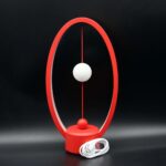 Horloge de bureau design moderne avec cadre ovale rouge, deux sphères blanches et rouges suspendues, et câble d'alimentation inclus, parfait pour la décoration scientifique et contemporaine.