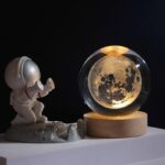 Globe lumineux représentant la lune avec figurine d'astronaute en plastique, décoration scientifique pour intérieur, ambiance spatiale et éducative.