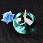 Bougie flottante en verre avec flamme allumée, posée sur une surface sombre.