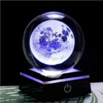 Lampe décorative en forme de lune dans une boule de cristal, illuminée d'une lumière bleue, posée sur un socle noir avec bouton d'alimentation.
