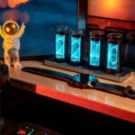 Dispositif de montreur de temps à tubes à décharge avec affichage lumineux bleu, placé sur une table en bois, avec un figurine d'astronaute à côté.