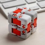 Cube puzzle mécanique en plastique blanc et rouge avec pièces interconnectées, posé sur un bureau avec clavier en arrière-plan.