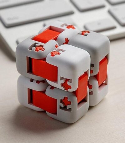 Cube puzzle mécanique en plastique blanc et rouge avec pièces interconnectées, posé sur un bureau avec clavier en arrière-plan.