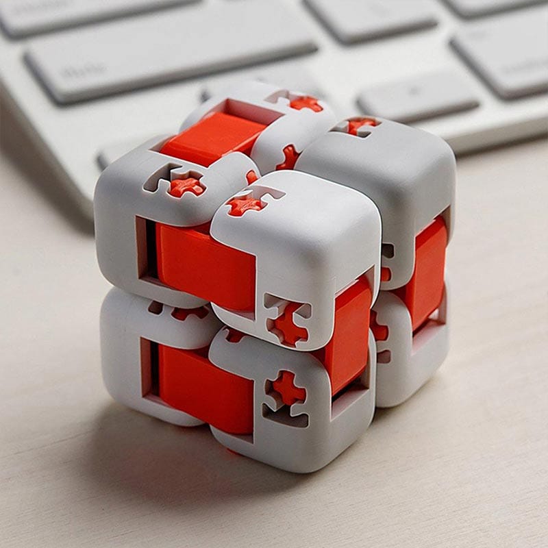 Cube puzzle mécanique en plastique blanc et rouge avec pièces interconnectées, posé sur un bureau avec clavier en arrière-plan.