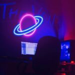 Panneau lumineux néon représentant une planète avec anneaux, dans un décor de laboratoire ou espace créatif.