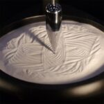 Pointe de stylo plongée dans un liquide blanc avec motifs tourbillonnants, illustrant un phénomène scientifique ou artistique.