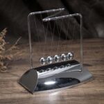 Pêndulo de Newton en métal brillant, objet scientifique décoratif pour bureau ou salon, illustrant les principes de la physique avec ses sphères suspendues.