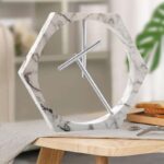 Horloge moderne en forme hexagonale avec cadre en marbre blanc et aiguilles en métal, idéale pour une décoration intérieure élégante et contemporaine.