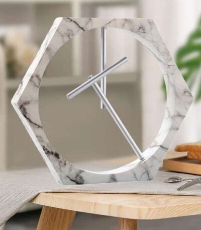 Horloge moderne en forme hexagonale avec cadre en marbre blanc et aiguilles en métal, idéale pour une décoration intérieure élégante et contemporaine.