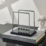 Pendentif Newton en métal brillant, modèle classique de la célèbre expérience de physique illustrant la conservation de l'énergie et la collision des corps. Parfait pour la décoration scientifique ou.