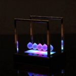 Panneau lumineux avec sphères de Newton suspendues, illuminées de couleurs changeantes, créant un effet visuel captivant.