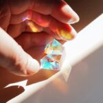 Prisme en cristal coloré tenu entre les doigts, créant des reflets lumineux et des jeux de couleurs.