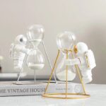 Réalisez une décoration originale avec ces figurines d'astronautes manipulant des sabliers en verre, symbolisant le temps et l'exploration spatiale.