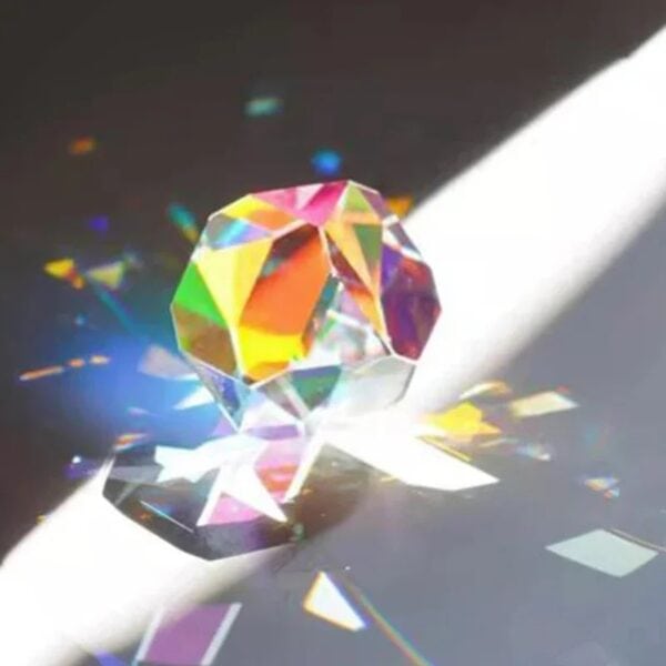 Pierre précieuse en cristal coloré avec reflets irisés, projetant des éclats de lumière multicolores sur une surface sombre.