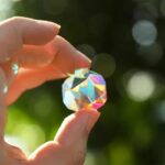 Cristal prismatique coloré tenu entre deux doigts avec un fond flou de nature.