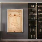 Illustration de l'Homme de Vitruve de Léonard de Vinci encadrée, exposée sur un mur gris, à cÎté d'une étagÚre noire contenant de la vaisselle et des objets décoratifs.