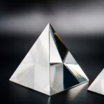Pyramide en verre optique avec surfaces réfléchissantes, utilisée comme objet décoratif ou scientifique, sur fond noir.