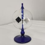 Pomme de Newton en verre avec poids en métal, objet scientifique décoratif, sur un fond blanc.