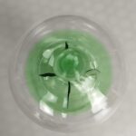 Pendentif en verre transparent contenant un liquide vert, avec un design scientifique et moderne, parfait pour la décoration ou comme accessoire original.